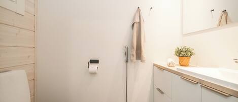 A bathroom with a toilet, a sink, a mirror, a towel rack, a potted plant, and a shower hose.