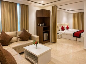 Habitación de hotel con sofá, una mesa de centro con un jarrón, cama con almohadas rojas, mesita de noche y armario.