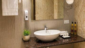 A bathroom with a marble sink, a towel rack, a mirror, a wall-mounted light, a potted plant, and toiletries.