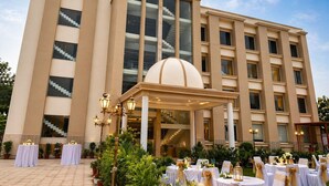 A hotel with a modern architectural design, featuring a central dome, large windows, and a spacious outdoor area with tables and chairs. - 8fold by LaRiSa, Basti (Basti)