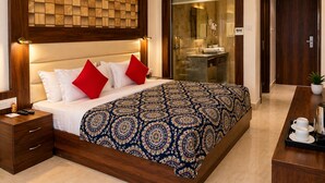 A hotel room with a large bed, a bedside table, a nightstand, a bathroom with a glass partition, and a wooden door. - 8fold by LaRiSa, Basti (Basti)