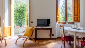 A cozy room with a wooden desk, a television, and a dining area with chairs.