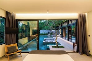 Un dormitorio moderno con una cama grande, televisor y vistas a una piscina y zona de estar exterior.