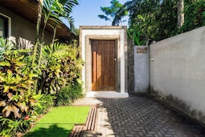 A gated entrance with a wooden door, a concrete wall, and a paved pathway leading to a building. - Villa Baoli by BaliSuperHost (Bali)