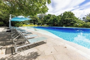 A swimming pool with lounge chairs and umbrellas, surrounded by greenery.