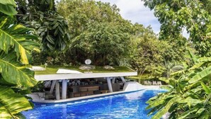 Un área de descanso junto a la piscina con diseño moderno, rodeada de exuberante vegetación.