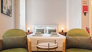 Et hotelværelse med en seng, to grønne lænestole, et rundt bord og et billede på væggen.
