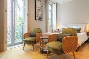Ein Zimmer mit einem Bett, zwei grünen Sesseln, einem kleinen Tisch und einem großen Fenster.