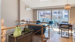 A modern living room with a wooden coffee table, blue chairs, and a large window offering a view of the city.
