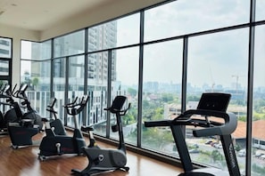 Une salle de sport équipée de matériel d’exercice et dotée de grandes fenêtres donnant sur un panorama urbain.