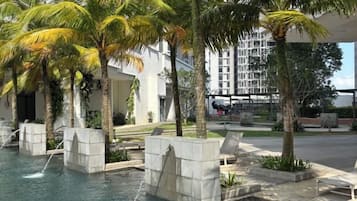 A pool area with water features and palm trees, surrounded by a modern building with a glass facade.