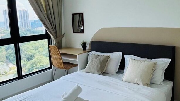 Habitación de hotel con cama, escritorio y silla. Se ve un ventanal con vistas a edificios y árboles.