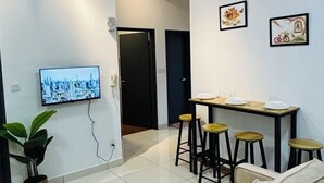 Una sala de estar moderna con una televisión, una mesa de comedor con taburetes y cuadros en la pared.