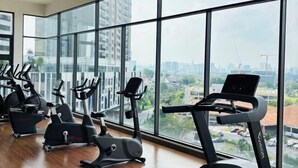 Un gimnasio con varias máquinas de ejercicio y amplios ventanales que ofrecen vistas a la ciudad.