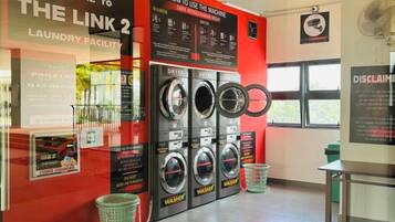A laundry facility with multiple washing machines, a wall-mounted fan, and informational posters.