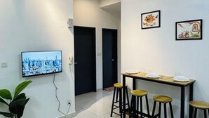 Una sala de estar moderna con un televisor de pantalla plana, una mesa de comedor con taburetes y dos puertas que dan a otras habitaciones.