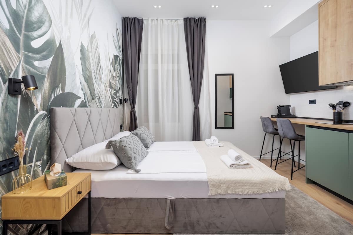 A modern hotel room with a bed, bedside table, and a small kitchenette.