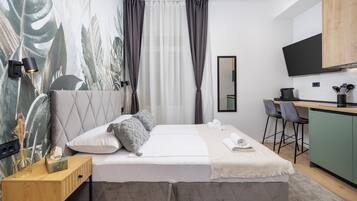 A modern hotel room with a bed, bedside table, and a small kitchenette.