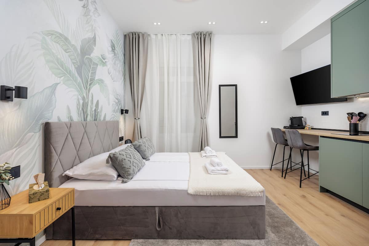 A modern bedroom with a large bed, a desk, and a kitchenette.