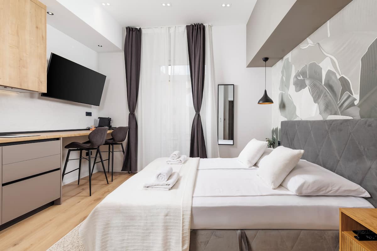 A modern hotel room with a bed, a desk, a chair, and a TV mounted on the wall.