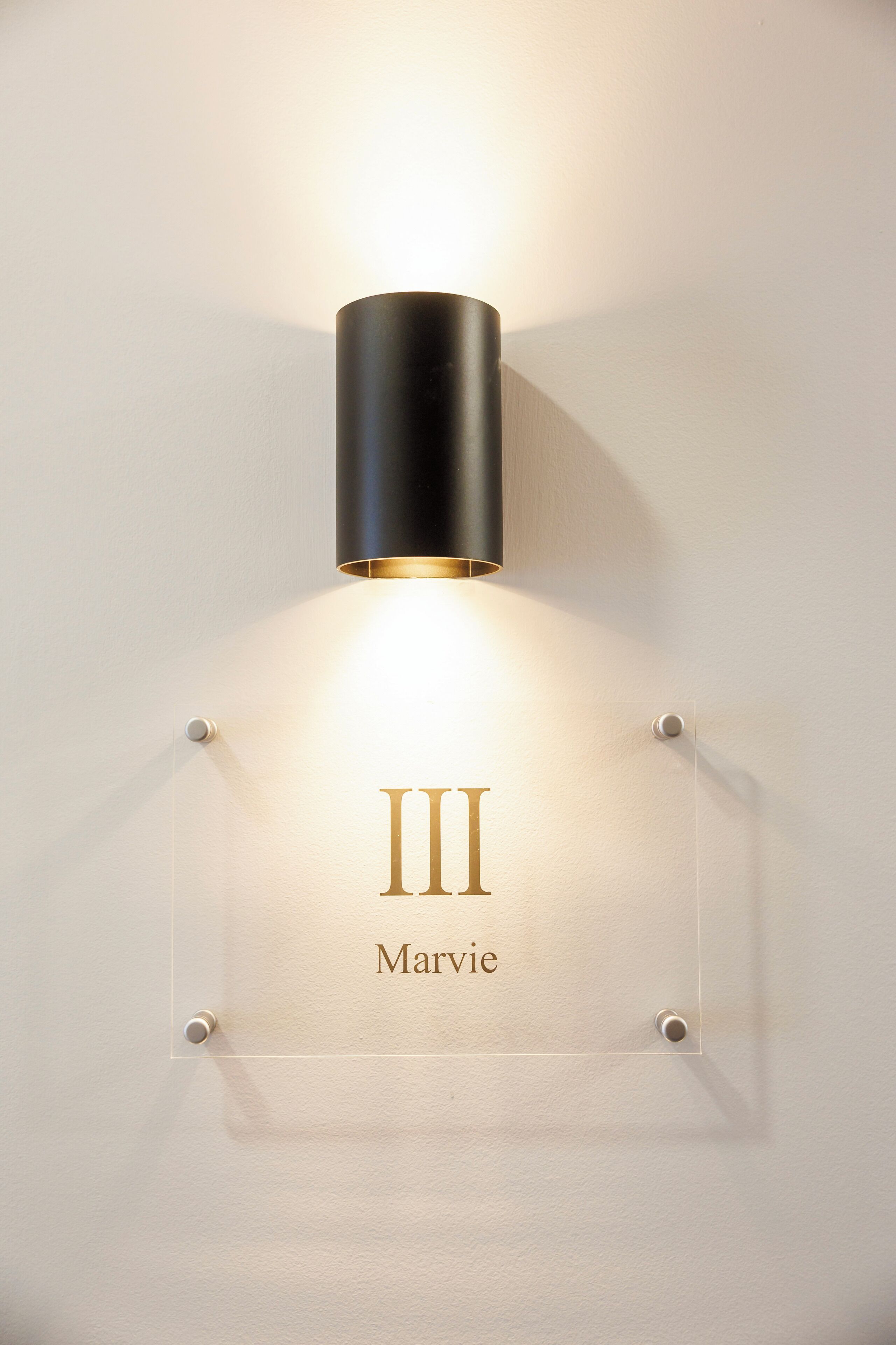 A wall-mounted light fixture with a clear nameplate reading "Marvie."
