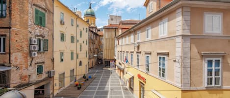 A narrow street with buildings on either side, a clear sky, and a few people walking.