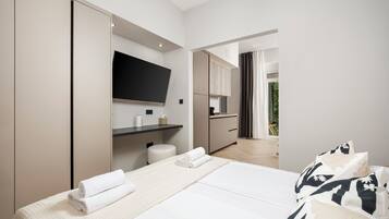 Una habitación de hotel moderna con una cama, un televisor montado en la pared, una pequeña cocina y vistas al exterior.
