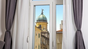 A view through a window with curtains, revealing a building with a green dome and a statue on top. - Marvie Apartments (Rijeka)