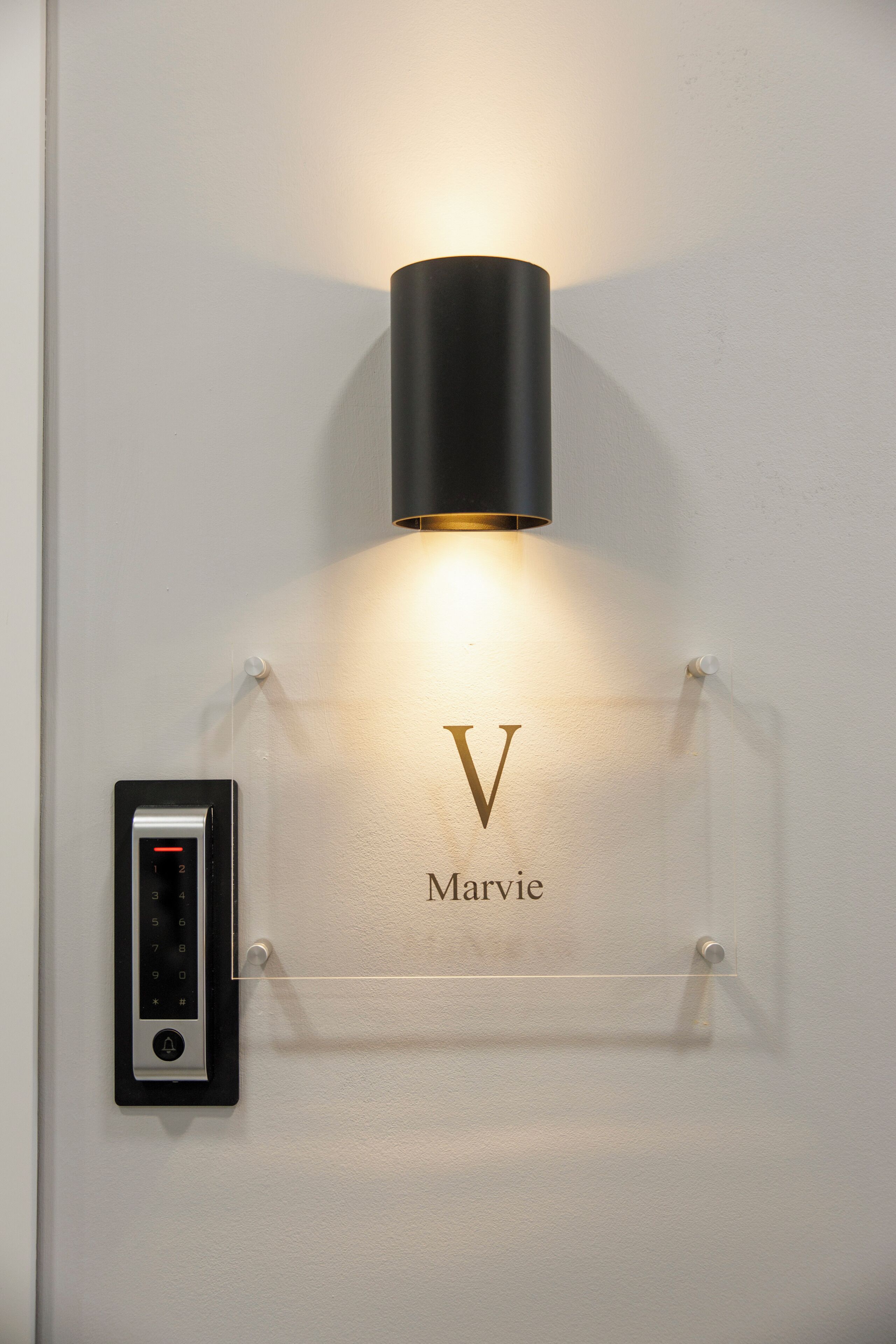A wall-mounted light fixture with a clear nameplate reading "Marvie" and a digital lock.