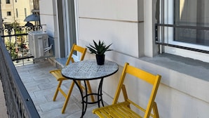 A balcony with a round table and two yellow chairs, a potted plant, and a view of adjacent buildings. - Marvie Apartments (Rijeka)