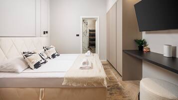 A modern bedroom with a large bed, a flat-screen TV mounted on the wall, and a small plant on a shelf.