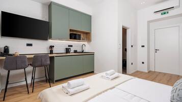 Une chambre d’hôtel moderne dotée d’un grand lit, d’une petite kitchenette, d’un téléviseur à écran plat et d’une porte signalée comme issue de secours.