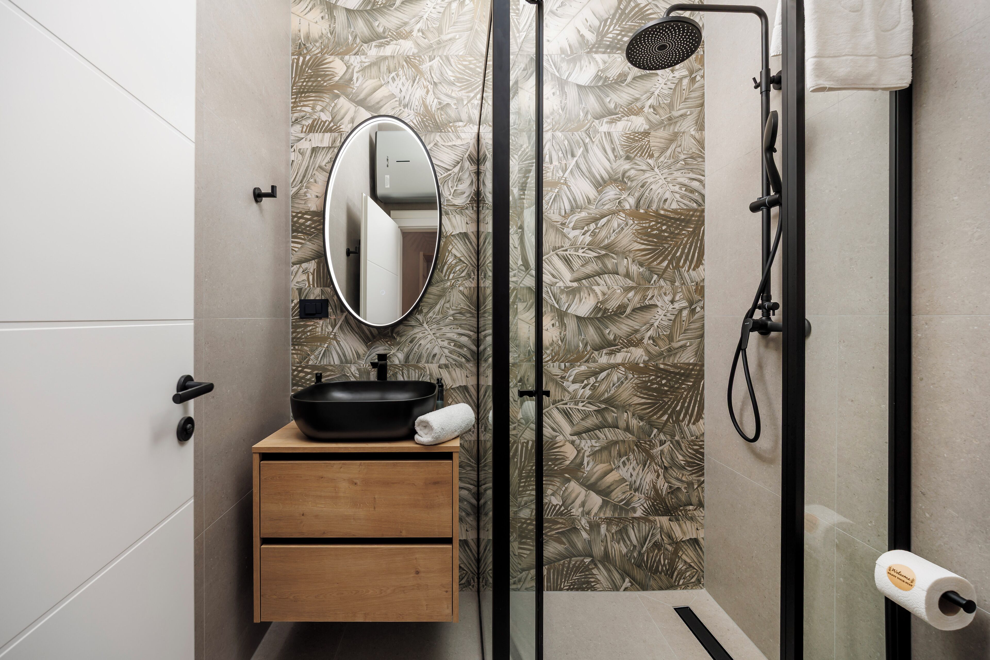 A bathroom with a wooden vanity, a black sink, a mirror, a shower with a handheld showerhead, and a toilet paper holder.