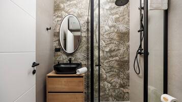 A bathroom with a wooden vanity, a black sink, a mirror, a shower with a handheld showerhead, and a toilet paper holder.
