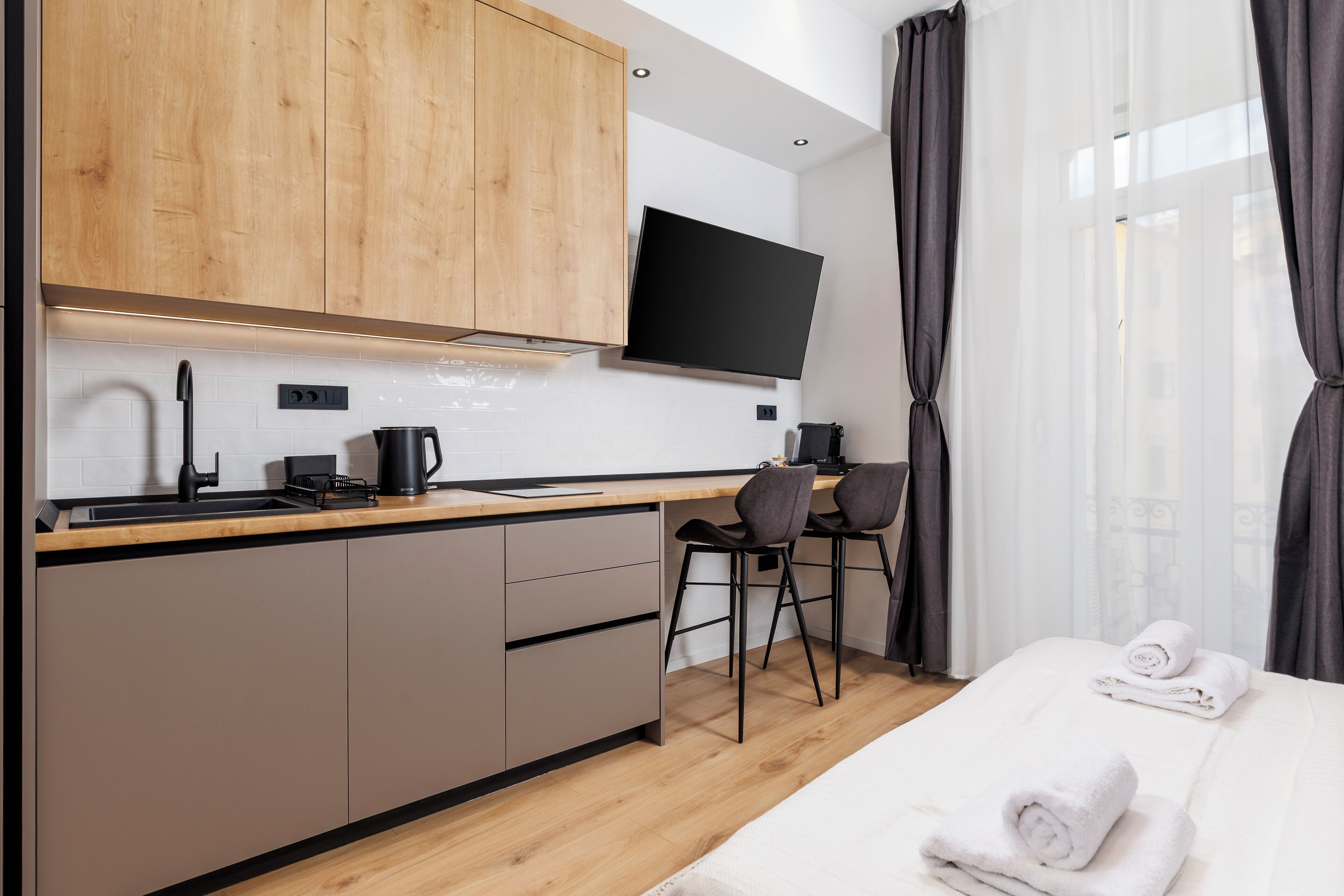 A modern kitchen with wooden cabinets, a black TV, and a dining area with two chairs.