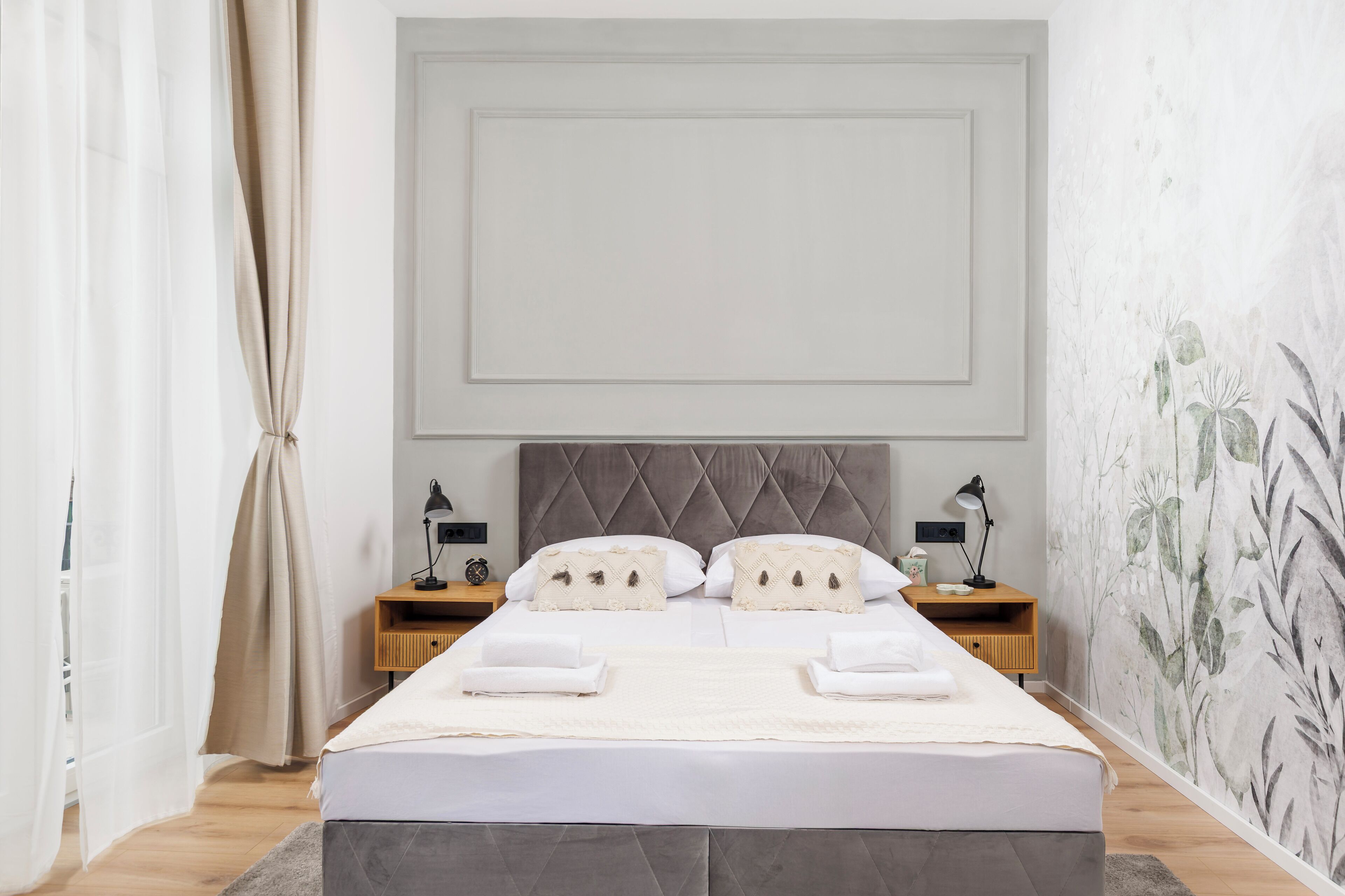 A neatly made bed with white linens, a tufted headboard, and two bedside tables with lamps.