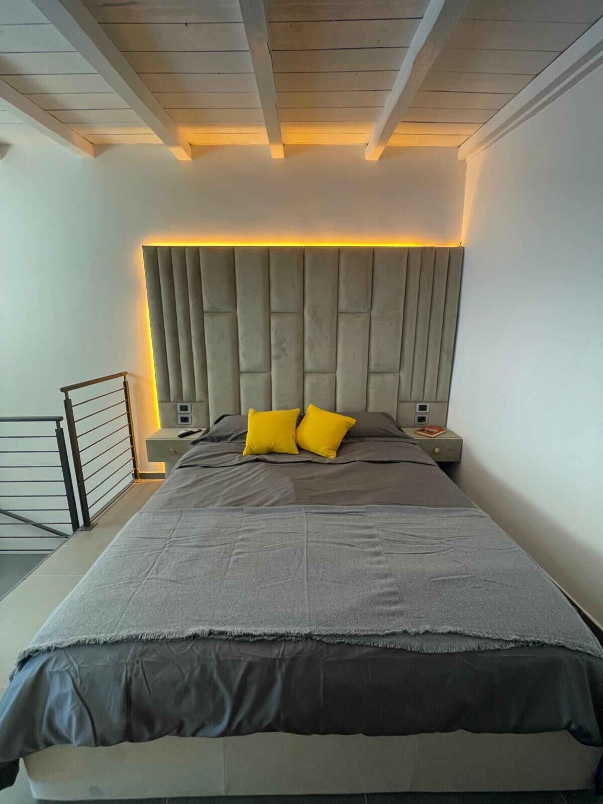 A modern bedroom with a large bed, a headboard with built-in lighting, and a nightstand with a lamp.
