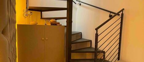 A modern staircase with a metal railing, a small cabinet, and a wall-mounted shelf with decorative items.