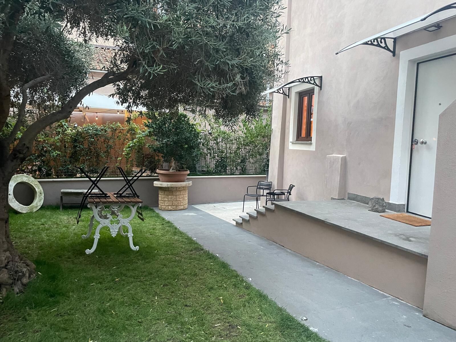 Un patio con una pequeña mesa y sillas, una planta en maceta y un banco de piedra.
