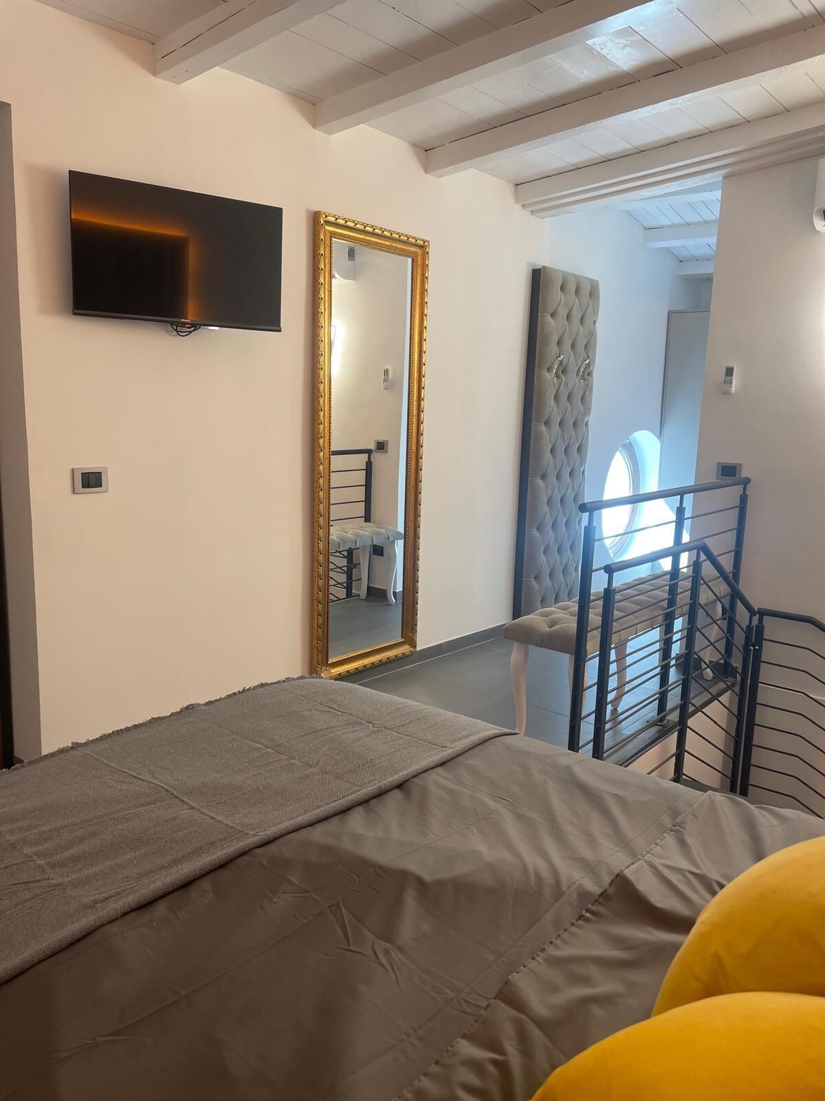 A bedroom with a bed, a large mirror, a TV, and a staircase leading to a balcony.