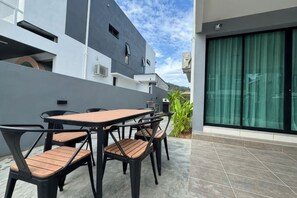 An outdoor patio with a table and chairs, a modern building in the background, and a large window with curtains. - Villa 19 Private Pool Langkawi (Langkawi)