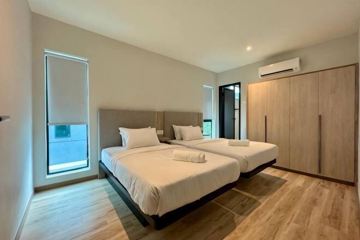 A bedroom with two beds, a wardrobe, and a large window.