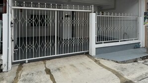 A white two-story house with a gated driveway and an air conditioning unit on the roof. - Lovely 3-bedroom house with AC in Minburi (Krung Thep Maha Nakhon)