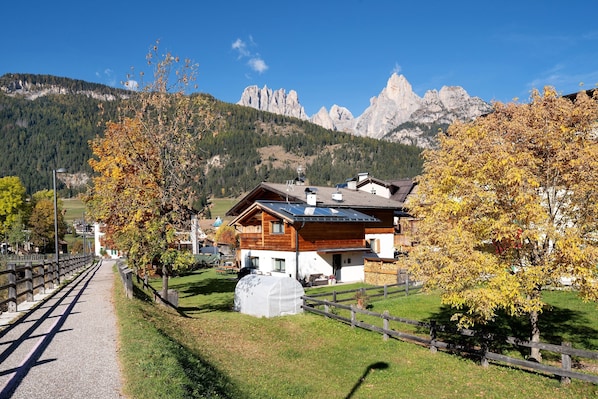 A mountain house with a wooden exterior, a covered outdoor area, and a view of rocky mountains.