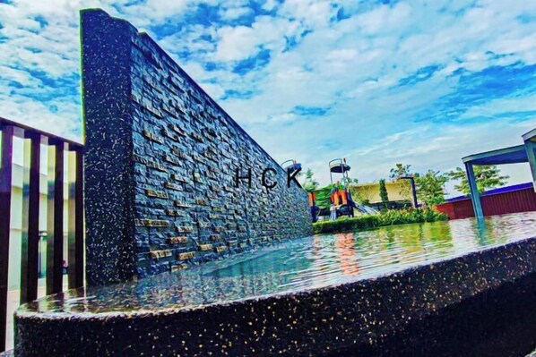 A modern building with a textured facade and a water feature in front. - Mall Suite at Sunsuria Setia Alam by HCK (Petaling)