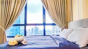 A hotel room with a large window, a bed with white pillows, and a rolled towel on the bed. - Mall Suite at Sunsuria Setia Alam by HCK (Petaling)