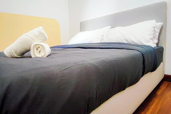 A neatly made bed with a grey bedspread and white pillows, a rolled white towel on the left side, and a wooden floor. - Mall Suite at Sunsuria Setia Alam by HCK (Petaling)
