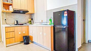 A compact kitchen with wooden cabinets, a black refrigerator, and a trash bin.