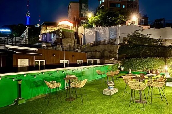 An outdoor seating area with tables and chairs, surrounded by a green hedge and a building with a staircase. - Look Home Guesthouse in Myeong-dong (Seoul)