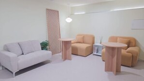 A modern living room with a white sofa, two beige armchairs, and two round wooden tables. - Look Home Guesthouse in Myeong-dong (Seoul)